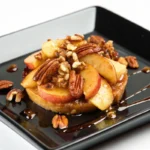 Fried apples with pecans and maple syrup on a black plate.