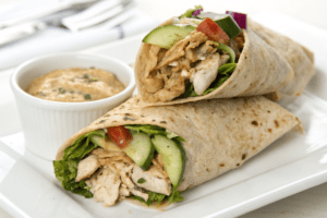 Mediterranean chicken wrap with hummus, lettuce, and cucumber served with tzatziki.