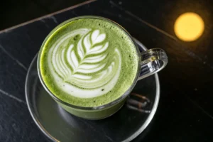 A glass mug holds a matcha latte with latte art on a dark, marbled surface.